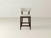 The Everly Upholstered Stool by James & James features a high-backed wooden design with a light-colored upholstered seat and backrest, showcasing mid-century charm against a plain, light background.
