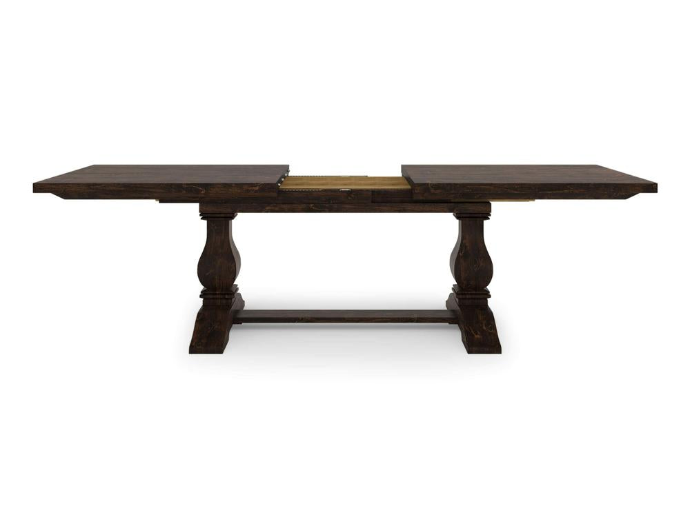 The Heirloom Expandable Dining Table - Tobacco by James+James is a wooden dining table with a dark finish, featuring a trestle base and two pedestal legs. It includes an extendable leaf section in the center, allowing you to extend the table's length.