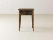 The Bennett 1 Drawer Nightstand by James & James is a small, rustic piece made from solid maple wood. It features a single drawer and slender legs, perfect for a bedroom, and is displayed against a plain, light-colored background.