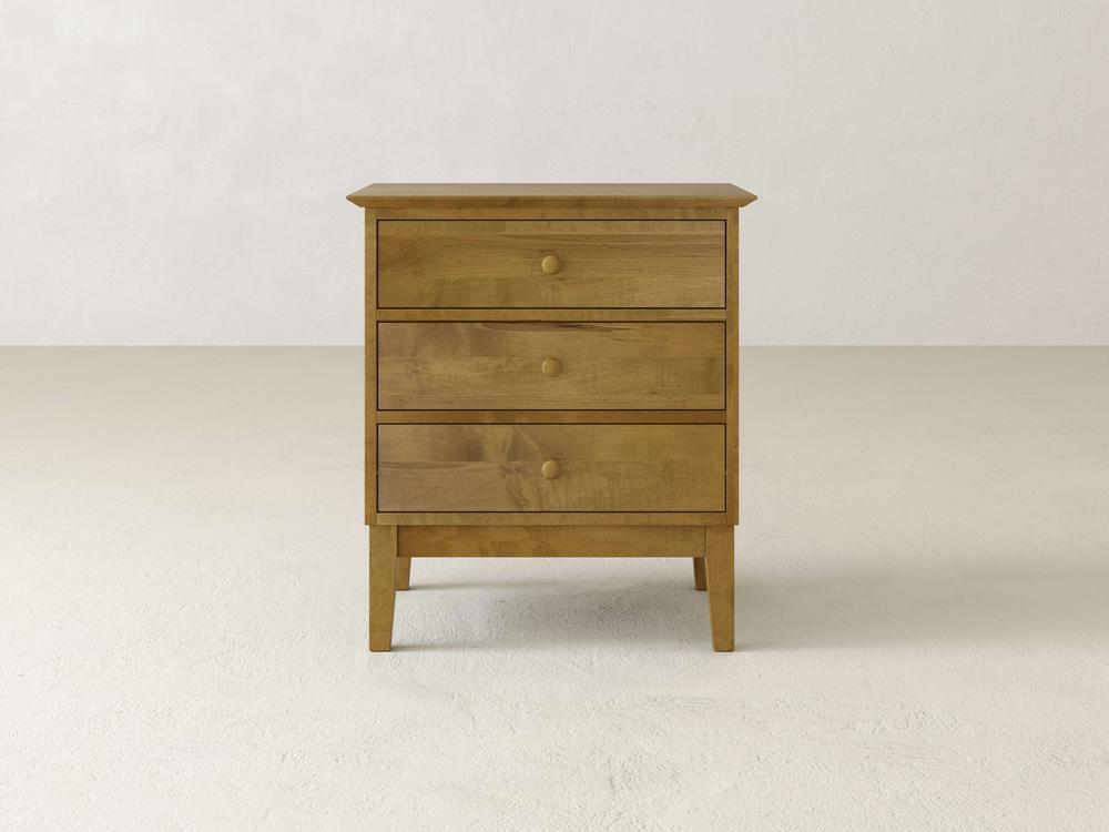 The Bennett 3 Drawer Nightstand by James & James, crafted from solid maple wood, features a minimalist design with round knobs and a natural wood finish, standing against a plain, light-colored background and blending simplicity with traditional elements.