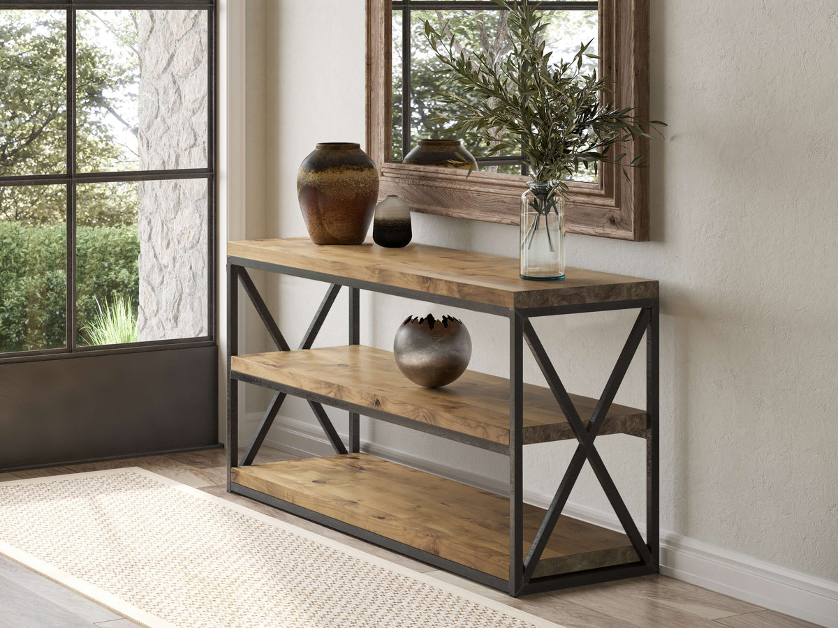 A wooden console table with black metal frame has three shelves, featuring decorative clay pots and a glass vase with olive branches. It is positioned near a large window and a wall mirror, with sunlight streaming in and a view of greenery outside.