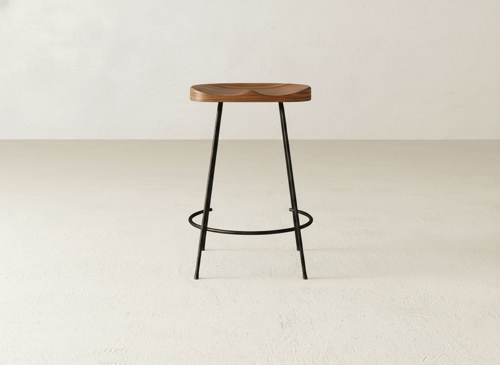 The Bryer Stool by James & James features a minimalist industrial design with a round wooden seat and slim black metal legs, all set against a light background for a simple, modern look.