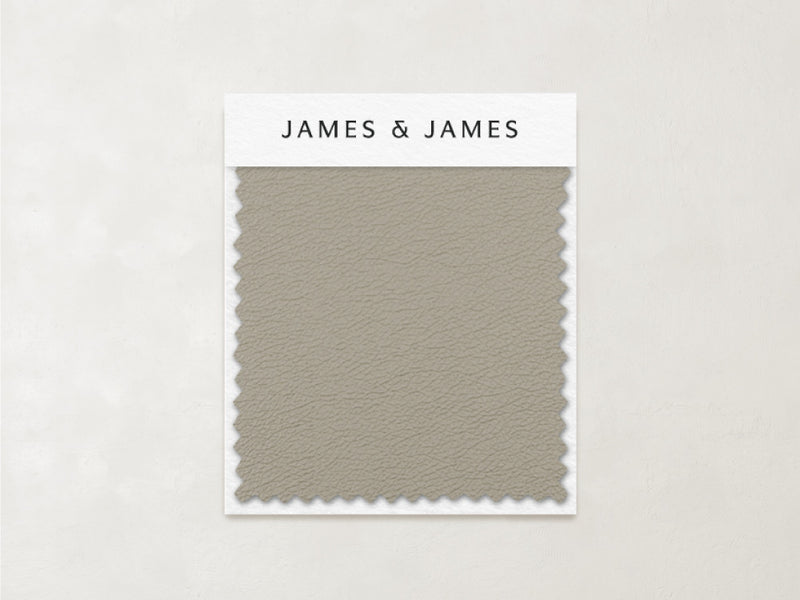 The Beige - Leather Swatch by James+James features a subtle, pebbled texture and zigzag-cut edges in muted taupe. Ideal for relaxed interiors, this soft Ultra Leather sample is labeled with the James+James brand at the top.