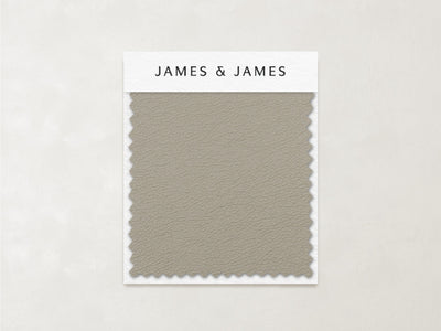The Beige - Leather Swatch by James+James features a subtle, pebbled texture and zigzag-cut edges in muted taupe. Ideal for relaxed interiors, this soft Ultra Leather sample is labeled with the James+James brand at the top.