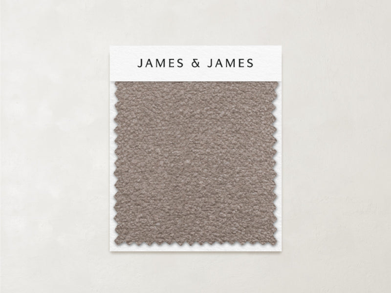A textured taupe Stone - Boucle Swatch by James+James with zigzag edges is mounted on a white card labeled "James+James." The light beige background highlights this cozy, timeless fabric—ideal for inviting, textured interiors.