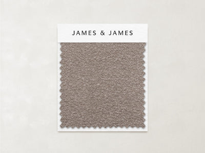 A textured taupe Stone - Boucle Swatch by James+James with zigzag edges is mounted on a white card labeled "James+James." The light beige background highlights this cozy, timeless fabric—ideal for inviting, textured interiors.