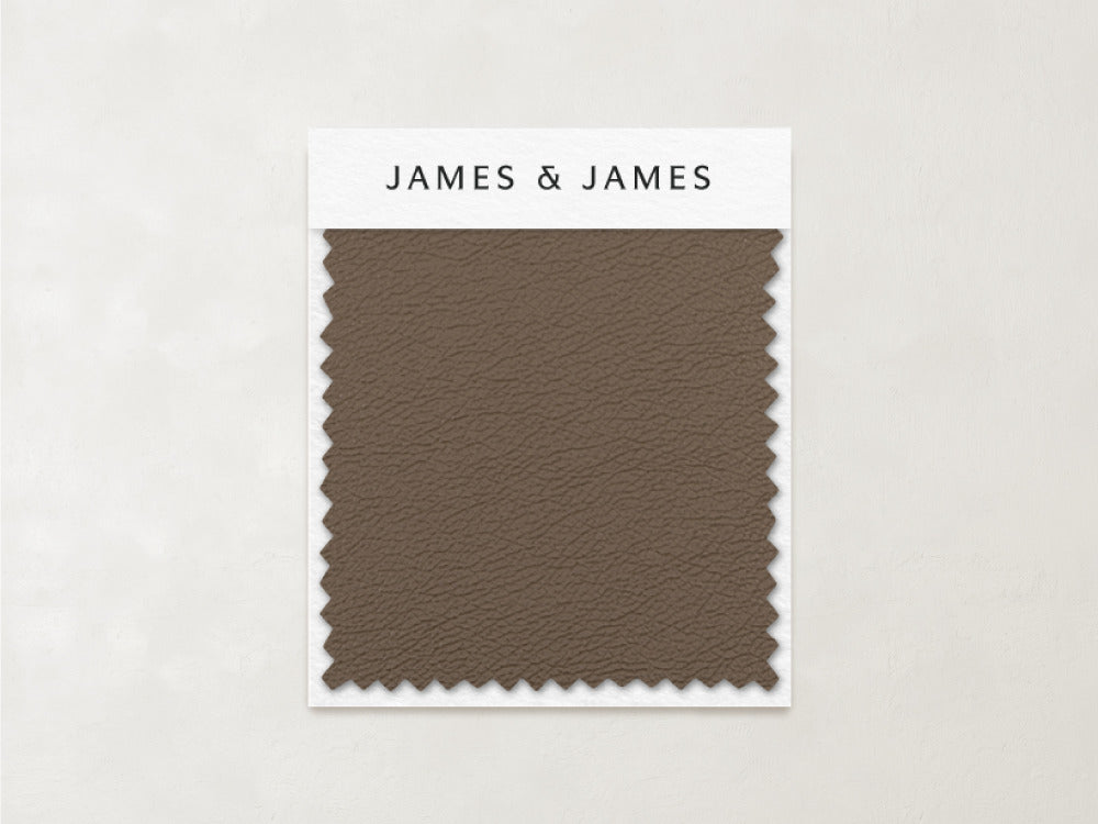 A rectangular sample of cool-toned brown leather, the Toffee - Leather Swatch by James+James, with zigzag-cut edges is attached to a card on a light beige background.