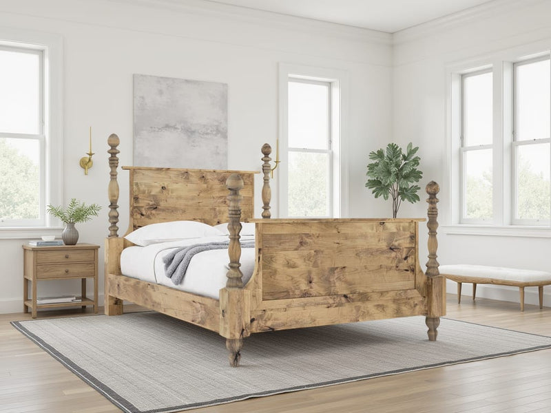 A bright, minimal bedroom features the James+James Catherine Bed in Harvest Wheat, white bedding, a wooden nightstand, a potted plant, and large windows filling the room with light. A rug accents the wooden floor.