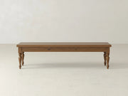 The James & James Chateau Bench - Almond on Oak features a rectangular wooden seat and four turned legs, shown against a plain, light-colored wall atop a pale floor.