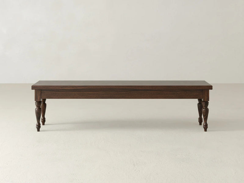 The James & James Chateau Bench - Sable on Oak features a dark rectangular top and four turned legs, set on a light-colored floor against a plain, light background.