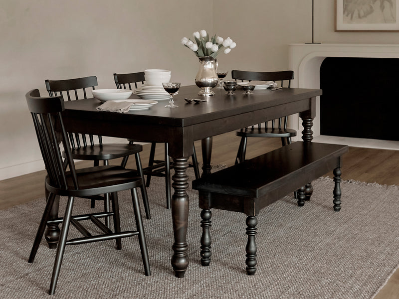 The James+James French Country Dining Table in Harvest Wheat, paired with matching chairs and a bench, sits on a textured rug. Set with plates, glasses, and white tulips, the room features neutral walls and minimal, elegant decor.