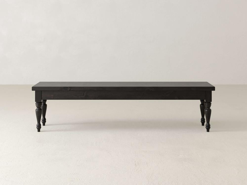 Against a plain white background stands the Chateau Bench by James & James, a long dark wooden piece with carved legs. This handcrafted bench offers a simple, classic design and four decorative legs, perfect for adding elegant dining seating that blends style and function.