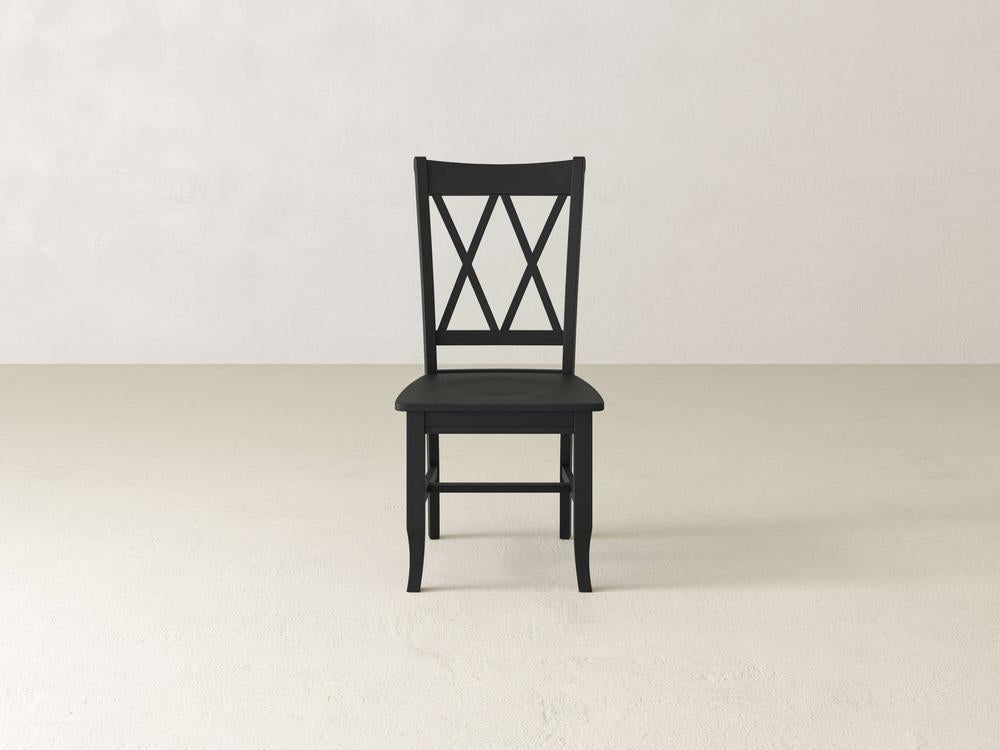 A black wooden chair with a decorative backrest featuring a crisscross pattern is placed on a plain, light-colored floor against a light wall.