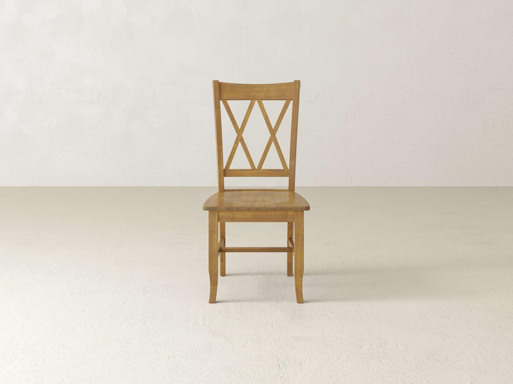 A wooden chair with a simple design is centered in an empty room with light walls and a plain floor. The chair has an X pattern on the backrest.