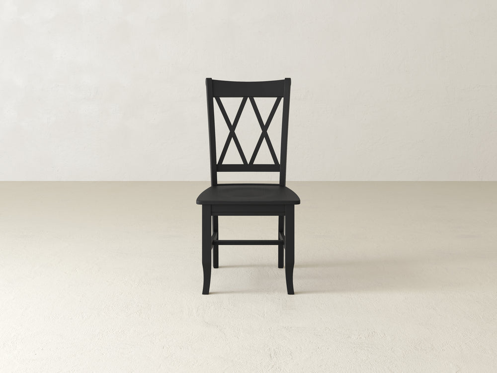 A wooden chair with a simple design is centered in an empty room with light walls and a plain floor. The chair has an X pattern on the backrest.