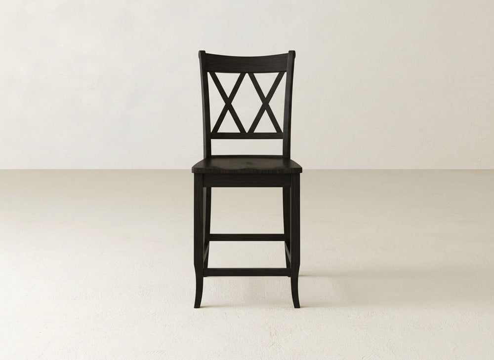 The James & James Double X Back Stool in black wood features a sturdy build and a crisscross "X" backrest, shown on a light floor against an off-white wall.