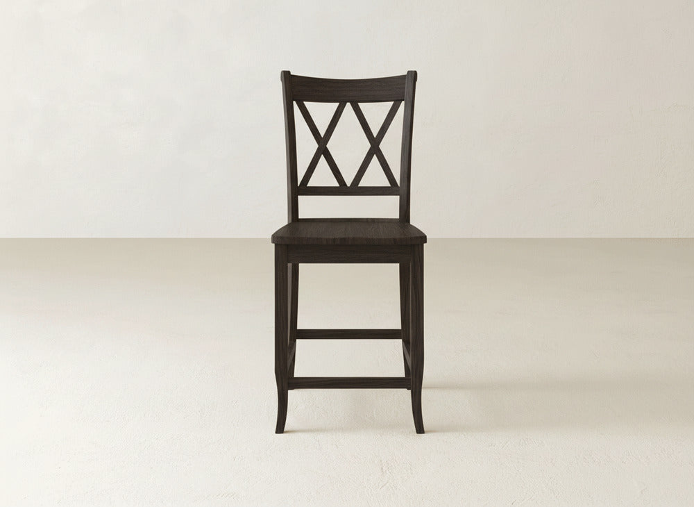 A James & James Double X Back Stool, featuring dark wood, a sturdy build, and a square seat, stands on a light floor against an off-white wall.