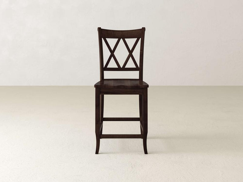 The Double X Back Stool by James & James, showcasing timeless elegance and superior craftsmanship, sits on a light-colored floor. Its backrest features a double "X" pattern and it has four straight legs against a plain, light-colored wall.