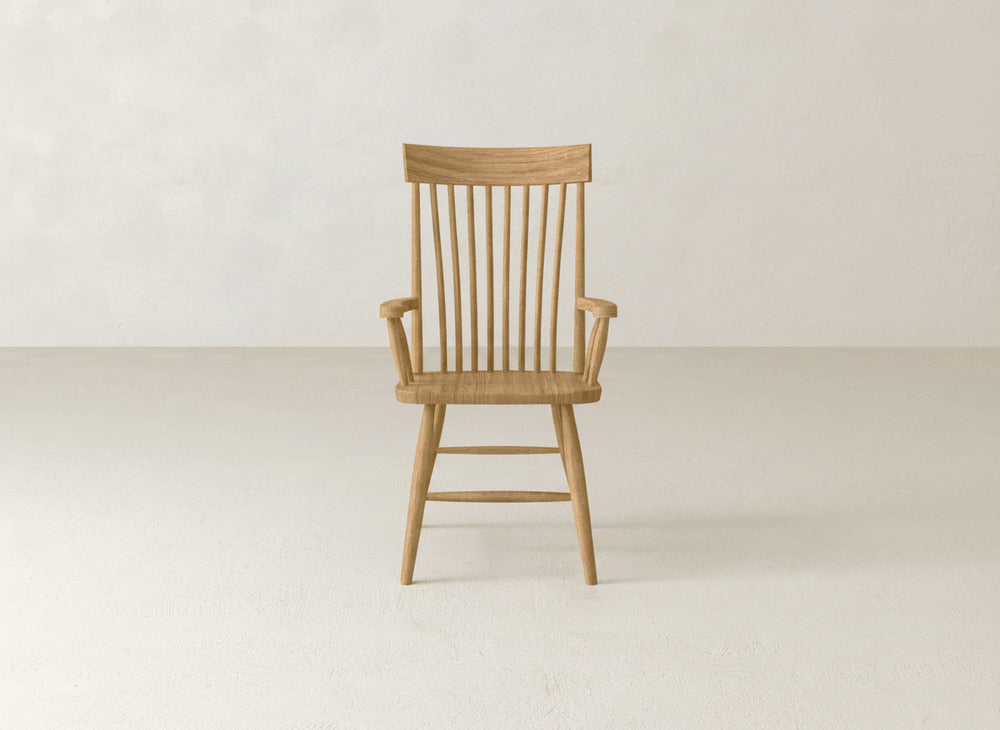 The Eleanor Arm Dining Chair by James+James, featuring a spindle back and armrests, sits on a smooth, light-colored floor against a plain, light wall.