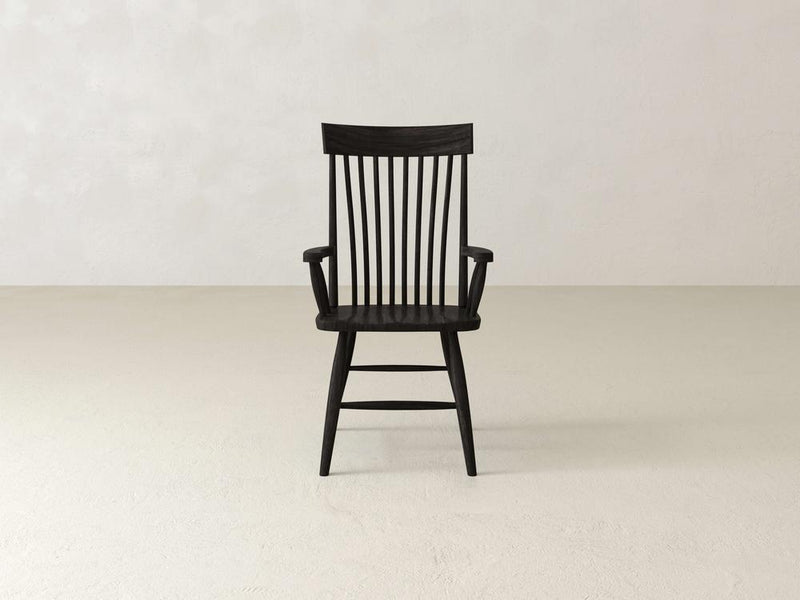 A dark wooden armchair with a high, vertical slatted back. The chair has curved armrests and a slightly angled seat. The design is simple and traditional, highlighting the natural wood grain.