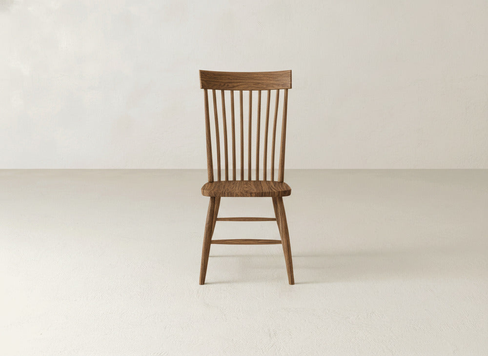 The James+James Eleanor Side Dining Chair, featuring a spindle back and simple solid wood design, sits on a light-colored floor against a plain off-white wall.