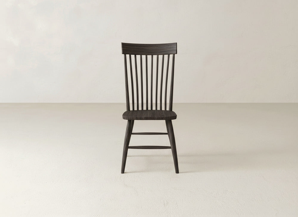 The Eleanor Side Dining Chair by James+James features a dark solid wood build with a spindle back and simple legs, shown on a light floor against a plain, off-white background.