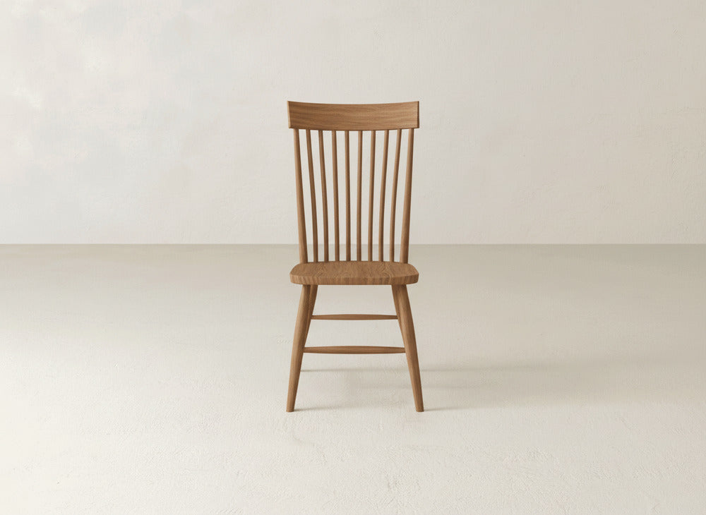The Eleanor Side Dining Chair by James+James, featuring a spindle back and simple solid wood design, sits on a light-colored floor against a plain off-white wall.