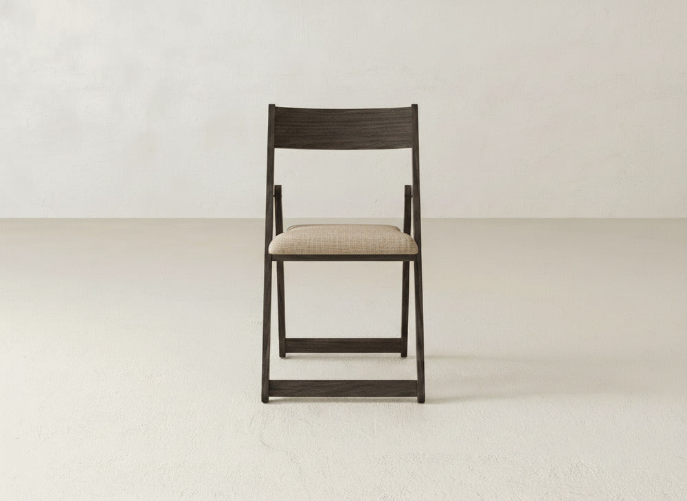 The Emmett Upholstered Folding Chair by James & James features dark wood and a beige cushioned seat, shown front-facing against a plain light wall and floor.