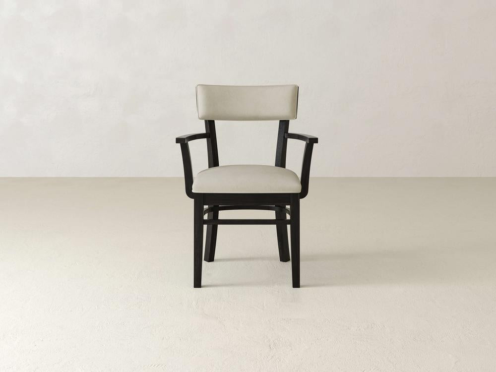 A wooden chair with light beige cushions on the backrest and seat is placed against a plain off-white background. The chair has armrests and dark-colored wooden legs.