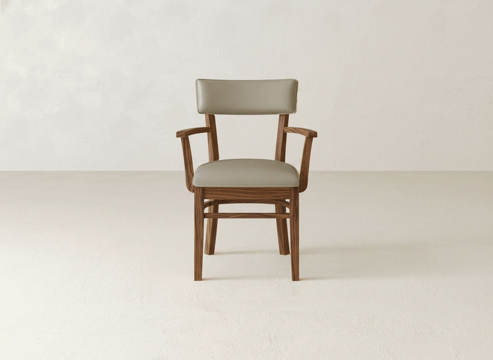 The Everly Arm Dining Chair by James+James features a modern upholstered design with a light brown padded seat and backrest, showcased at the center of a minimalist, light-toned room.