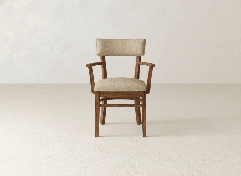 The Everly Arm Dining Chair by James+James showcases mid-century modern style with a beige upholstered seat and backrest, armrests, and is displayed against a plain light background.