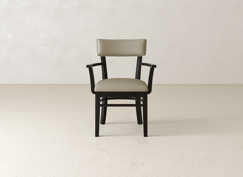 The Everly Arm Dining Chair by James+James features a modern, minimalist design with a dark wooden frame and beige upholstered seat and backrest, shown on a light floor against an off-white wall.