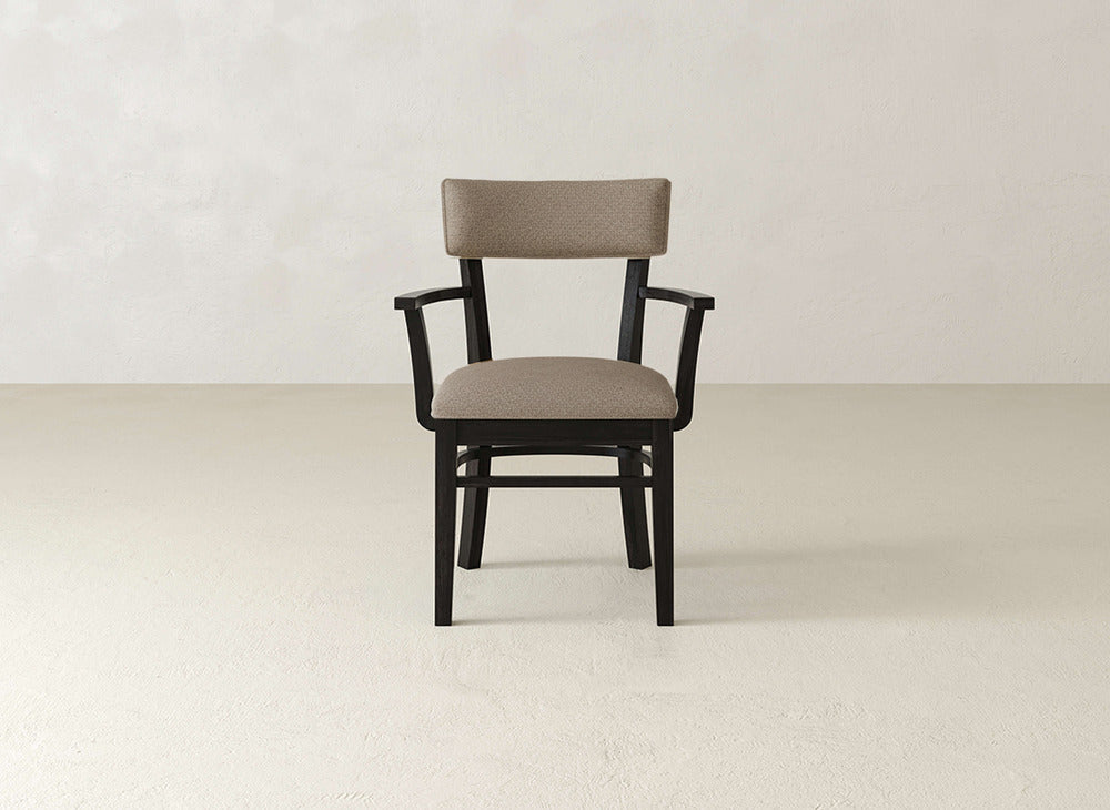 The James+James Everly Arm Dining Chair features a modern upholstered brown seat and backrest with black armrests and legs, centered against a plain, light-colored background.