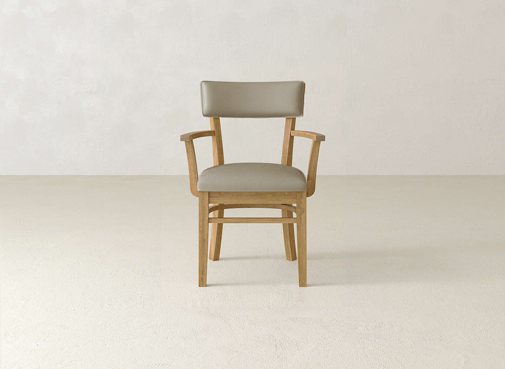The Everly Arm Dining Chair by James+James features a mid-century modern design with light brown wooden legs and frame, padded armrests, and beige cushioned seat and backrest, set against a plain light-colored background.