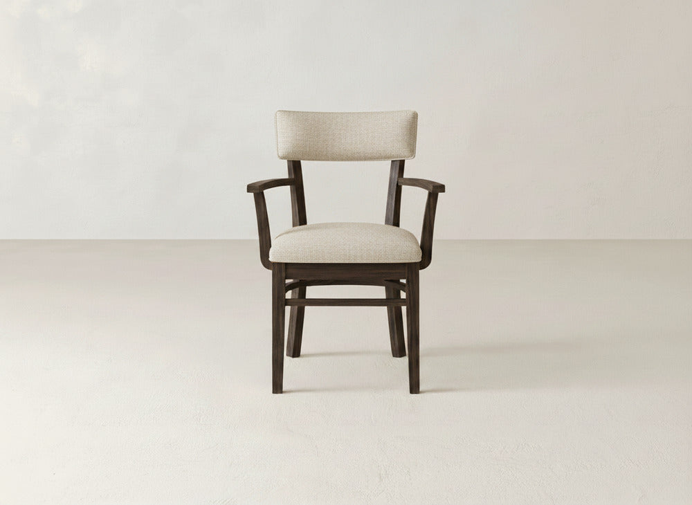 The Everly Arm Dining Chair by James+James features a light beige upholstered seat and backrest, showcased on a light floor with an off-white background for a modern, minimalist look.