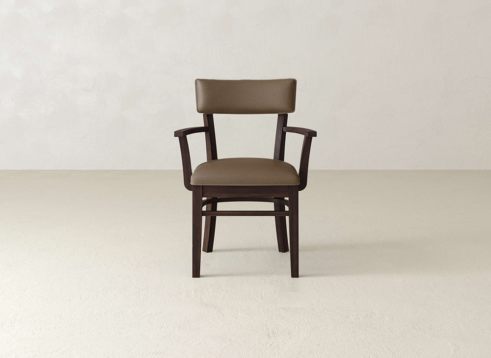 The Everly Arm Dining Chair by James+James features a brown padded seat and backrest, wooden armrests, and angled legs, shown against a plain beige background.