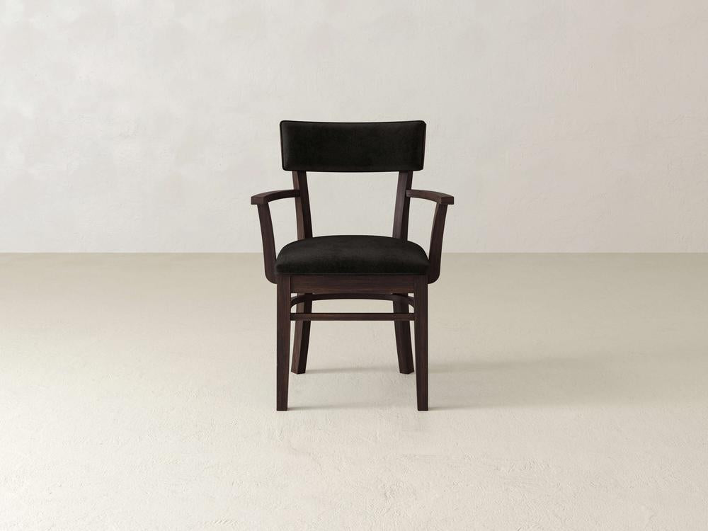 A black cushioned wooden chair with armrests is centered against a plain light gray background. The chair has a simple, sleek design with a slightly curved backrest.