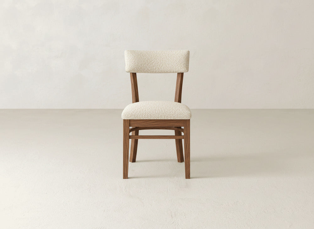 The Everly Side Dining Chair by James+James features a wooden frame with a light, textured upholstered seat and backrest, shown on a plain, light floor against a neutral wall.