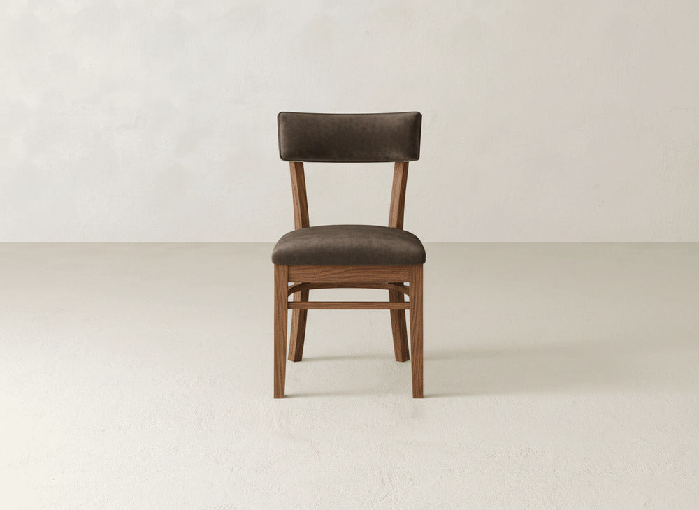 The Everly Side Dining Chair by James+James features a dark brown cushioned seat and backrest, set on a plain light-colored floor against a neutral off-white wall.