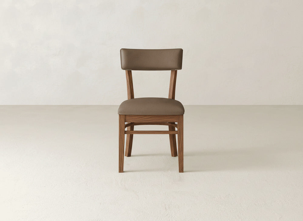 The James+James Everly Side Dining Chair, featuring a brown upholstered seat and backrest, is centered in a minimal, light-colored room with plain walls and floor.