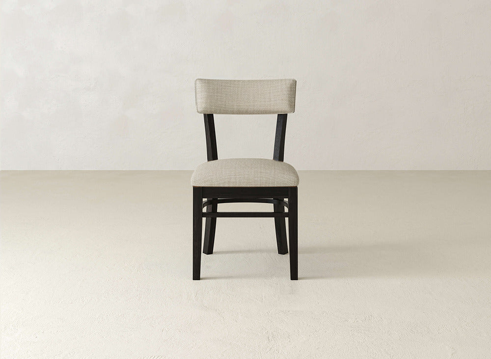The Everly Side Dining Chair by James+James features a light beige padded seat and backrest, black frame, and four straight legs, shown centrally in a simple, light-colored room with minimal background.
