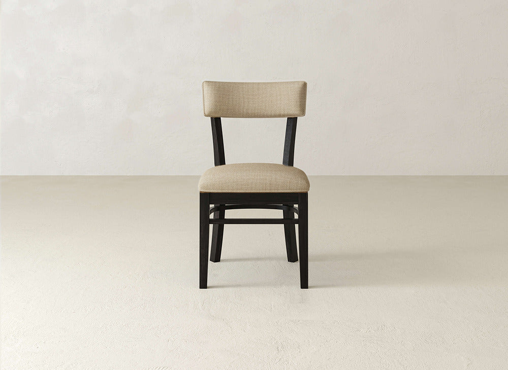 The Everly Side Dining Chair by James+James, featuring a beige cushioned seat and backrest, is centered against a plain, light-colored background.