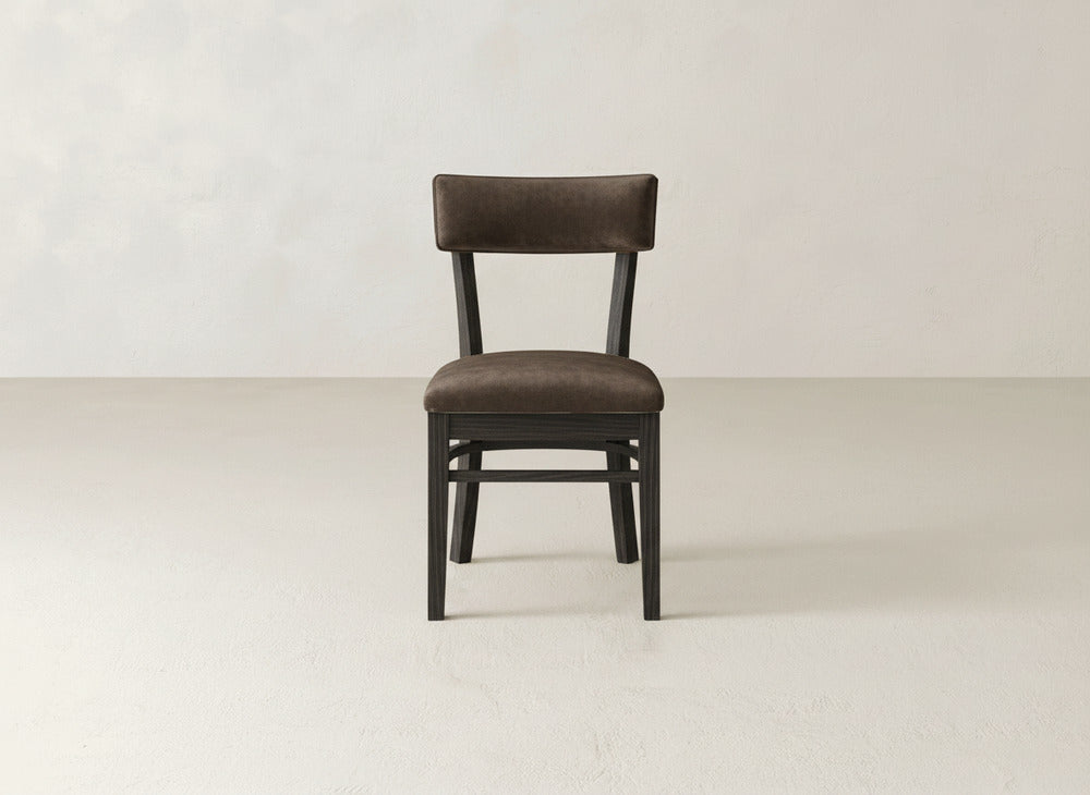 The Everly Side Dining Chair by James+James, featuring upholstery and a dark wooden frame, is centered on a light floor against an off-white wall, facing forward.