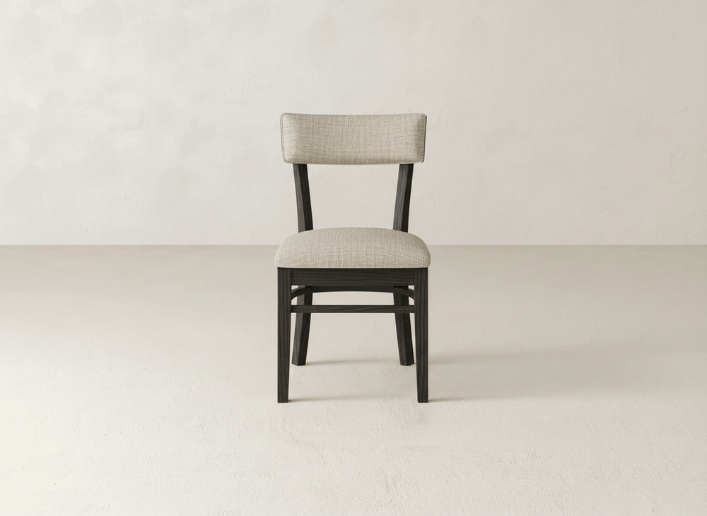 The Everly Side Dining Chair by James+James features an elegant design with a light beige cushioned seat and backrest, centered on a plain, light-colored floor against a neutral, textured wall backdrop.