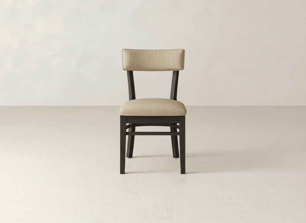 The Everly Side Dining Chair by James+James features a dark wooden frame and light beige upholstered seat and backrest, shown on a light floor against an off-white wall.