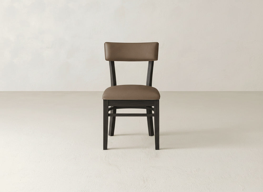 The Everly Side Dining Chair by James+James features brown upholstery, a simple modern design, and dark wooden legs, centered against a plain light-colored background.