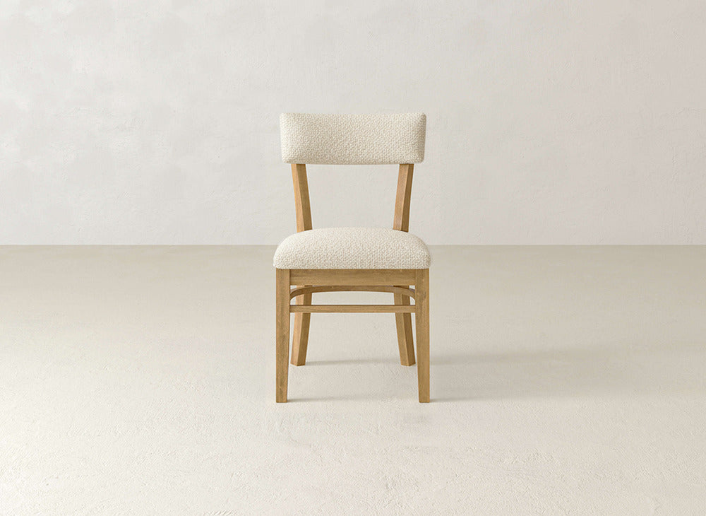 The Everly Side Dining Chair by James+James features light, textured upholstery on the seat and backrest and is centered in a minimalist room with neutral walls and floors.