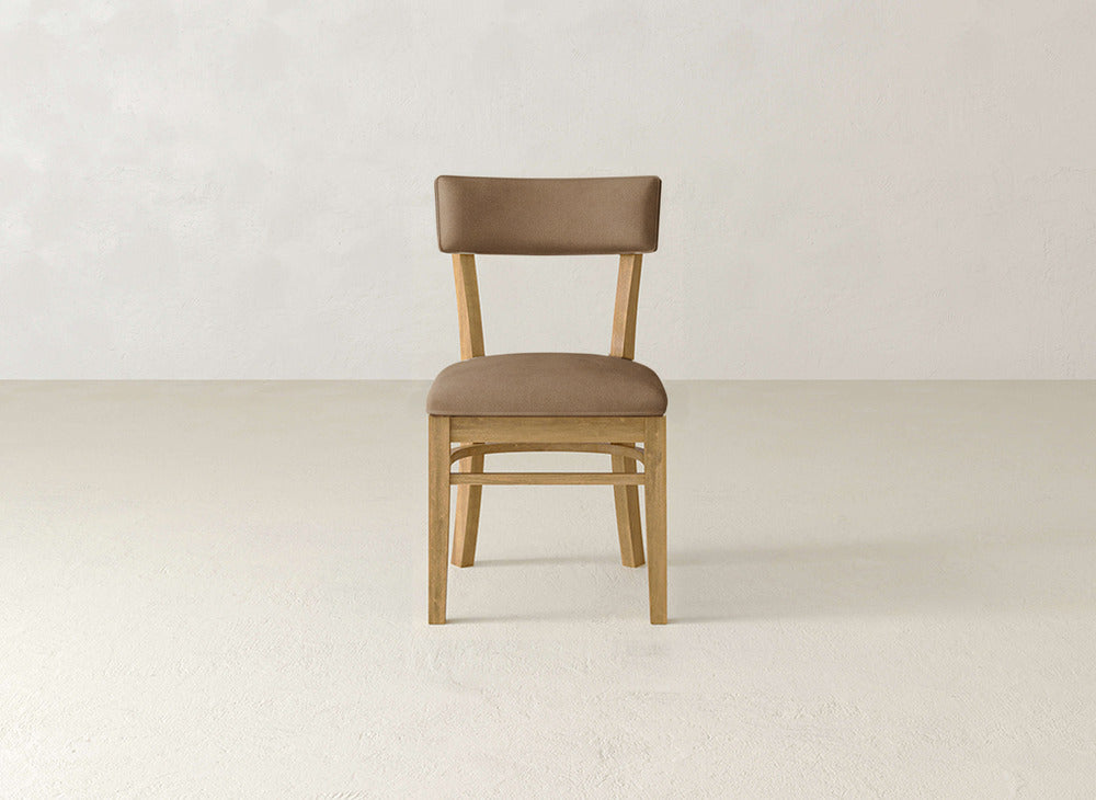 The Everly Side Dining Chair by James+James, featuring a light brown cushioned seat and backrest, sits centered on a light-colored floor against an off-white wall.