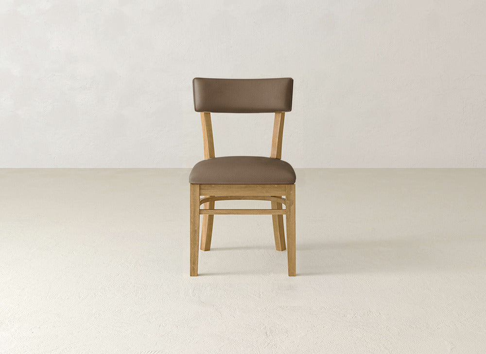 The Everly Side Dining Chair by James+James, featuring a padded brown seat and backrest, is centered on a light-colored floor against an off-white wall.