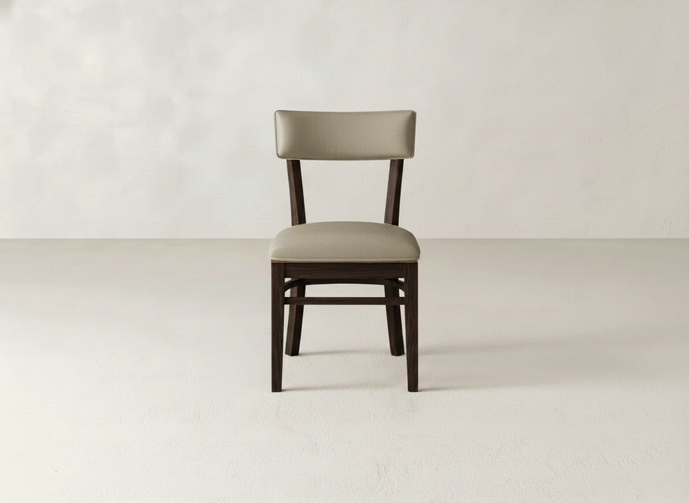 The Everly Side Dining Chair by James+James, featuring a padded beige seat and backrest, is centered in an empty room with light-colored walls and flooring.